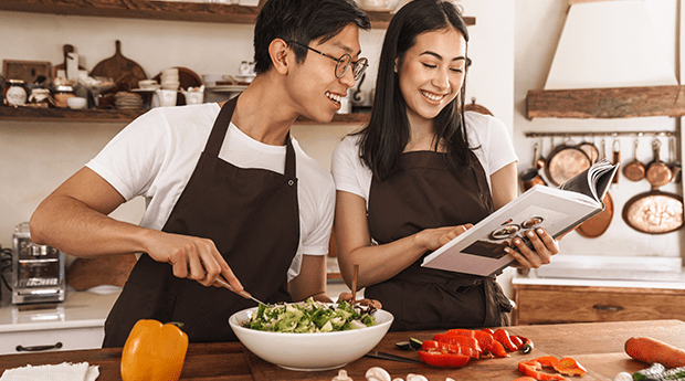 2 chefs looking at a recipe book while preparing food in a restaurant