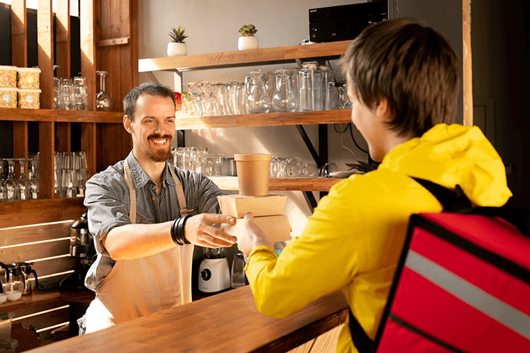 Restaurant staff handing over order to food delivery personnel