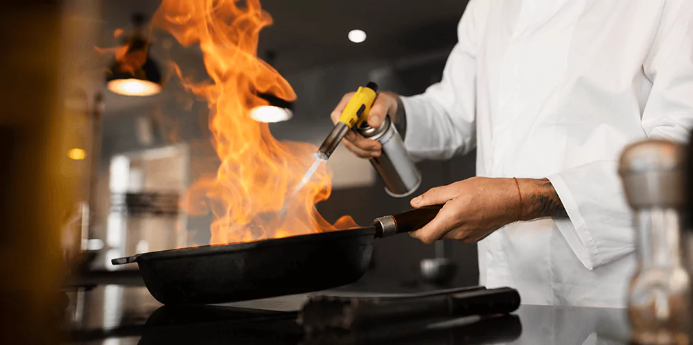 Kitchen staff using a kitchen blowtorch on a pan